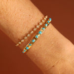 Two gold bracelets with turquoise stones on a wrist against a brown background