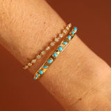 Two gold bracelets with turquoise stones on a wrist against a brown background