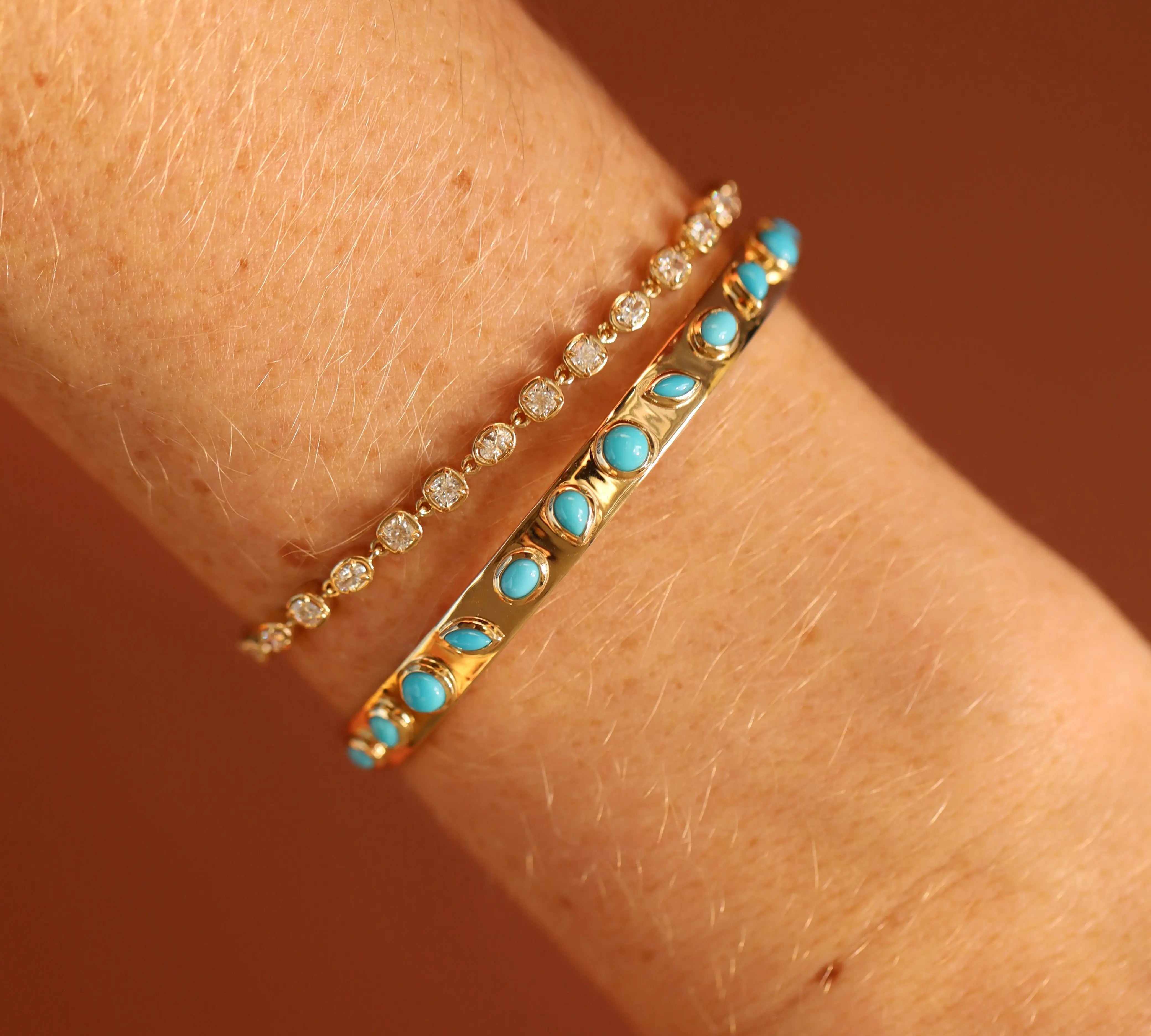 Two gold bracelets with turquoise stones on a wrist against a brown background