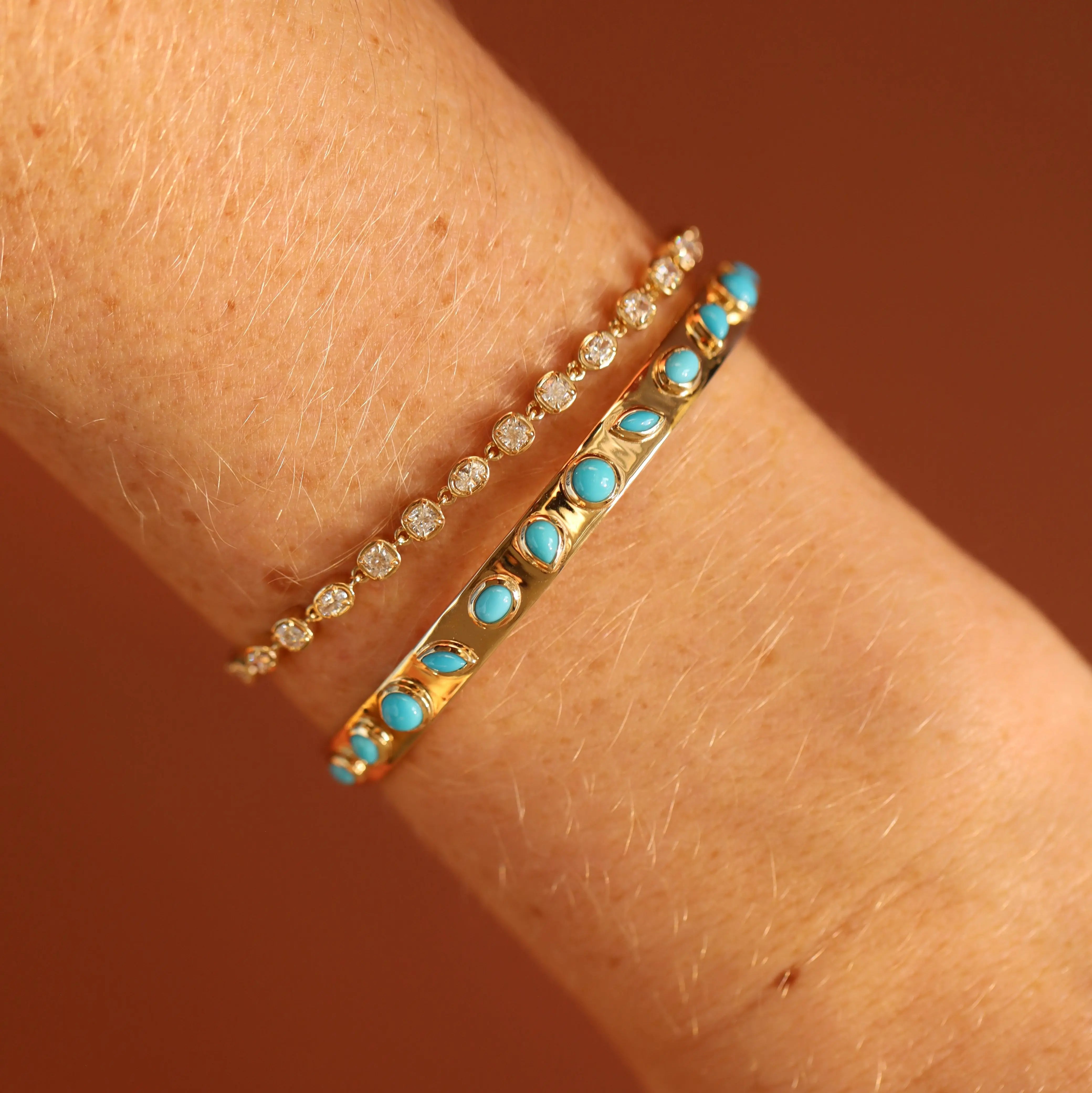 Two gold bracelets with turquoise stones on a wrist against a brown background