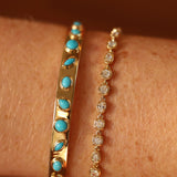 Two gold bracelets with turquoise stones and diamond accents on a wrist.