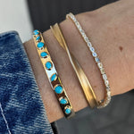 Close-up of a wrist wearing three bracelets. One with turquoise stones, a gold twist bracelet, and a diamond tennis bracelet.