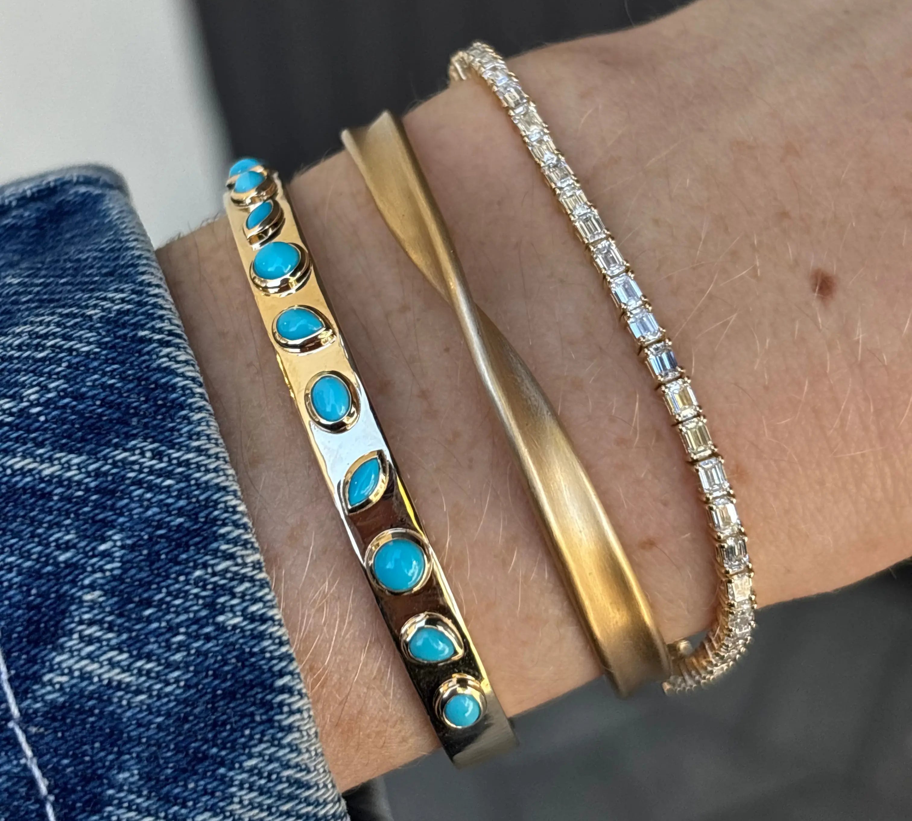 Close-up of a wrist wearing three bracelets. One with turquoise stones, a gold twist bracelet, and a diamond tennis bracelet.