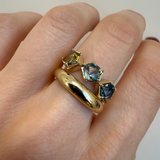 Gold ring with gemstones on a finger against a neutral background