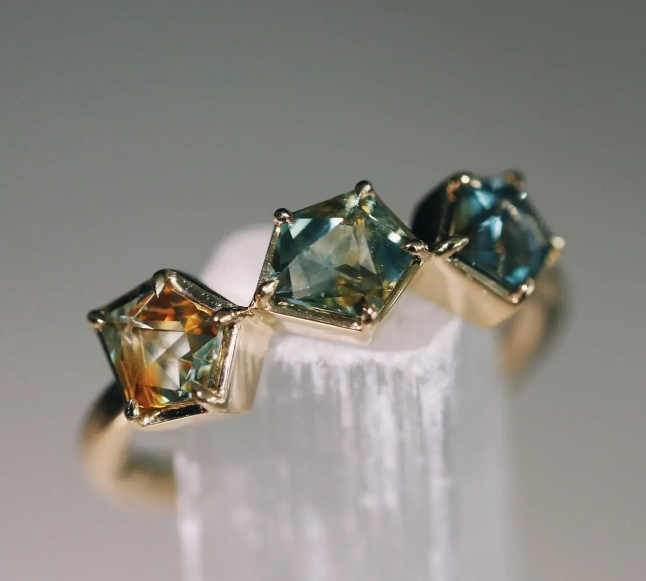 Gold ring with three green gemstones on a white stand against a gray background