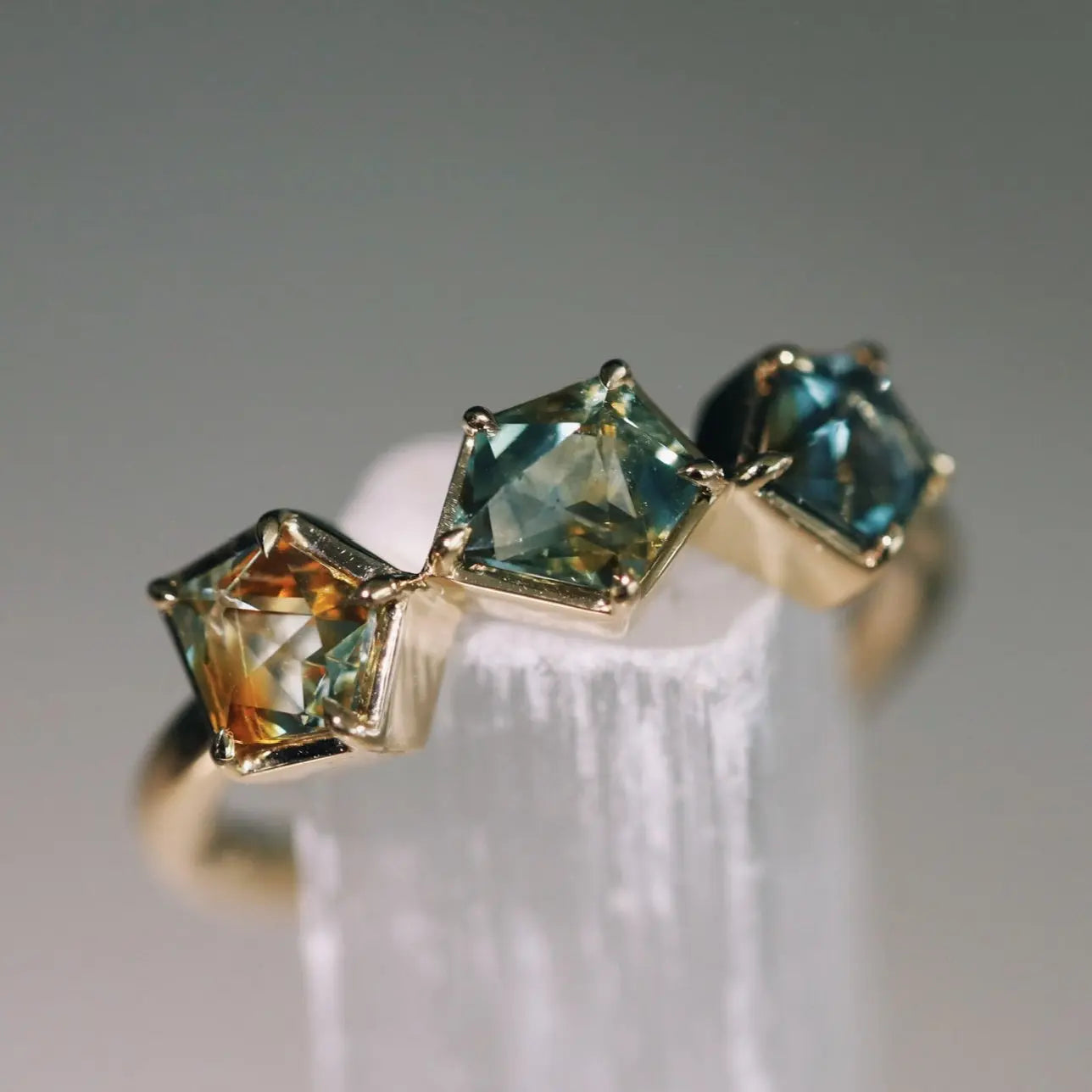 Gold ring with three green gemstones on a white stand against a gray background