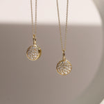 Two gold necklaces with round, diamond-studded pendants on a neutral background.