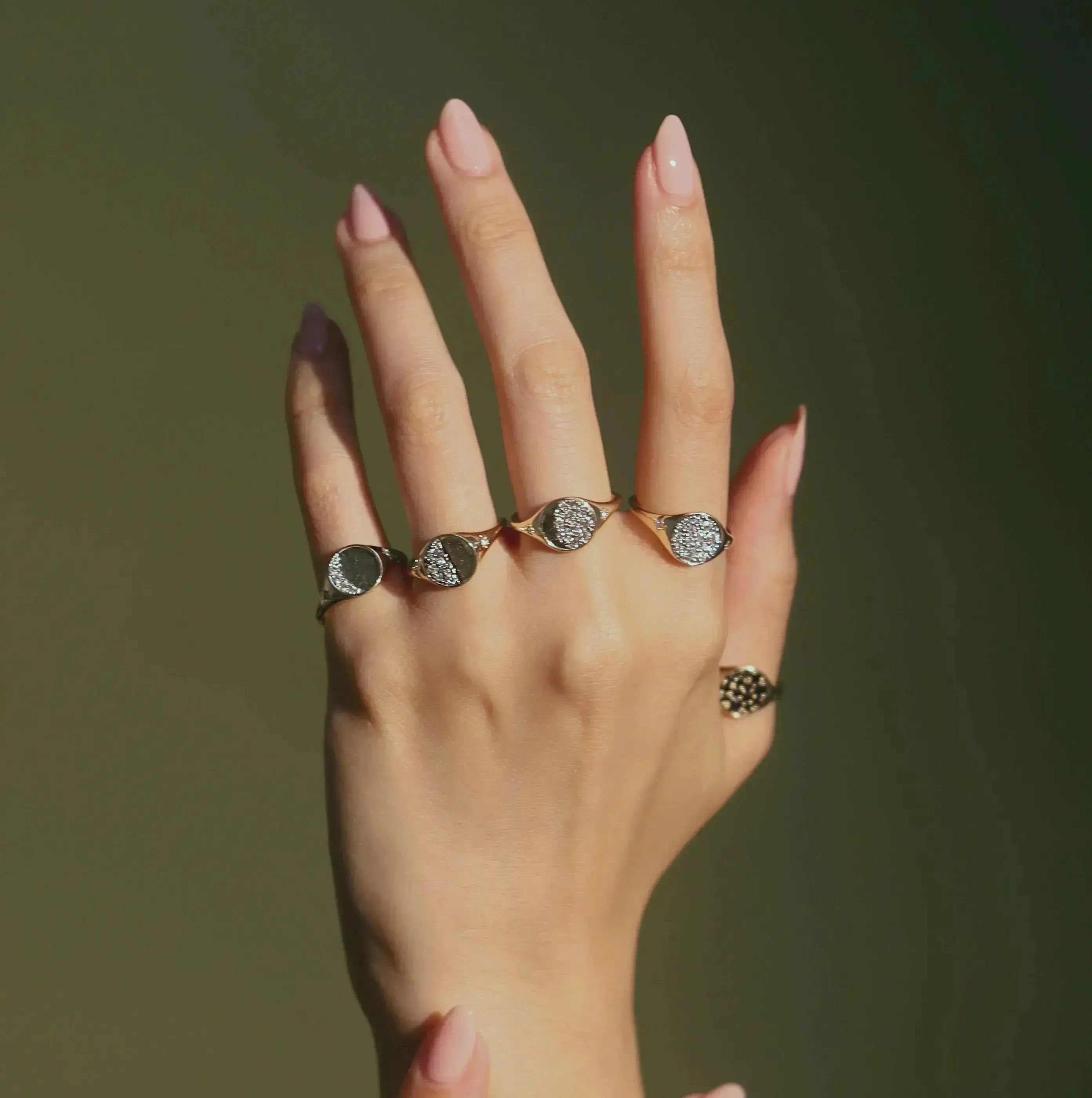 Close up of hand against a green background, featuring all Marrow Fine Moon Phase Signets