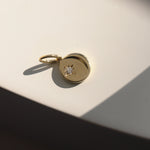 Gold pendant with a diamond on a light beige surface