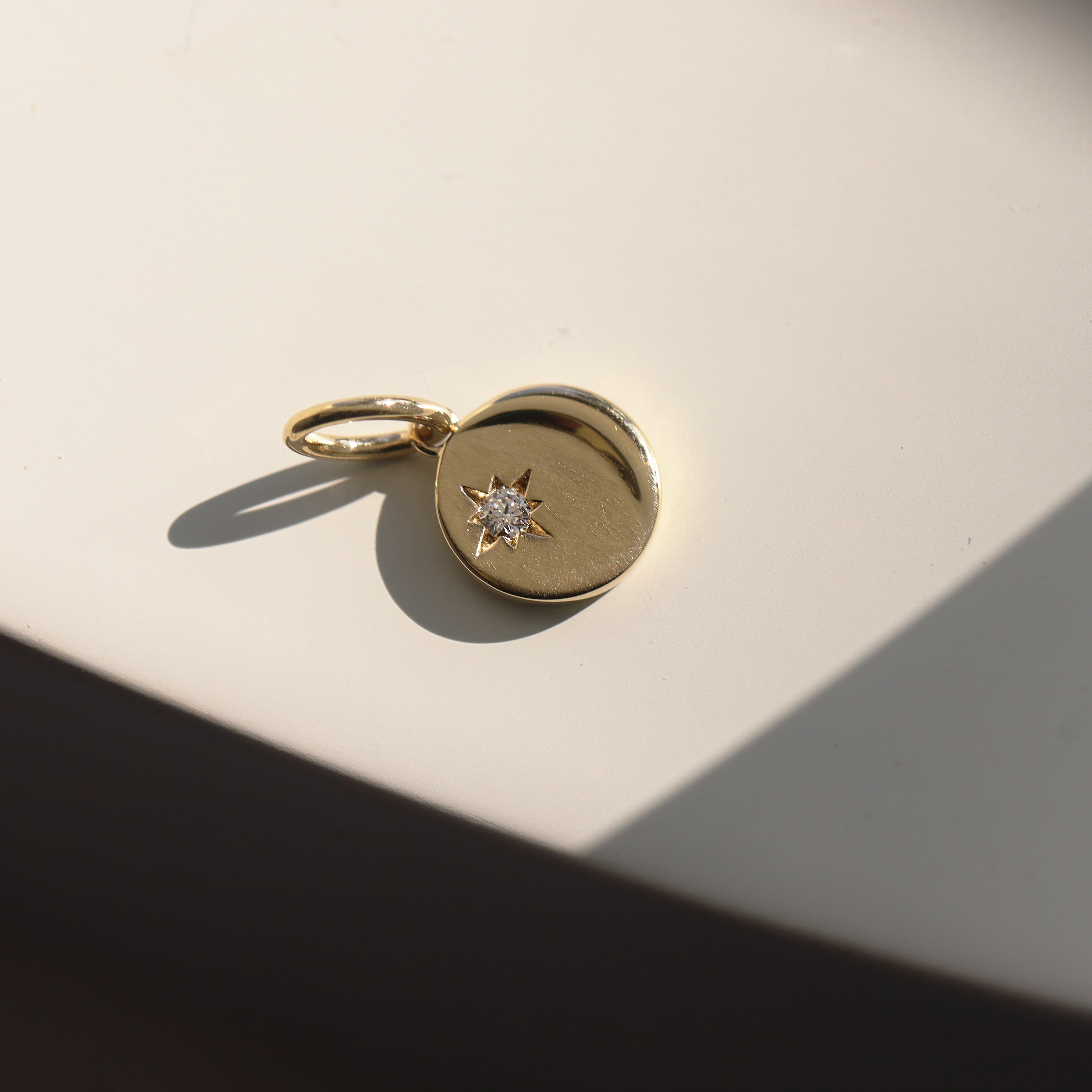 Gold pendant with a diamond on a light beige surface