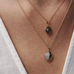 Two gold necklaces with pendant charms on a person's neck against a neutral background