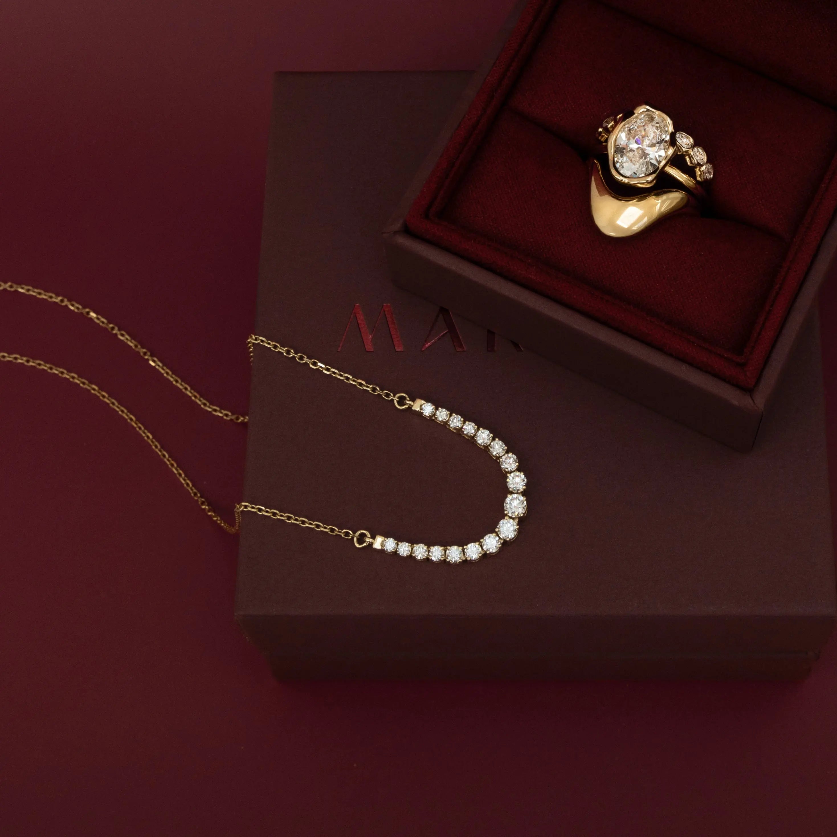 Naomi White Diamond Graduated Necklace draped across a burgundy jewelry box holding a diamond ring stack