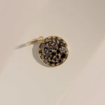 Gold pendant with black gemstones on a beige background