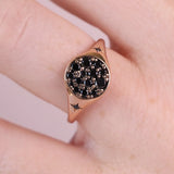 A close-up of a rose gold signet ring with a black pavé center and small clear accent stones, worn on a person's finger.