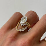 A close-up of a hand wearing a yellow gold ring set with a large oval diamond and smaller accent diamonds on a plain light background.