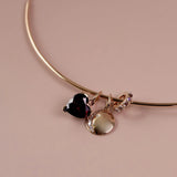 A gold collar necklace with three dangling charms: a dark red heart, a gold disc with moonstones and a small gold crescent with purple stones, set against a solid dusty pink background.