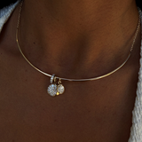 A close-up of a person's neck wearing a delicate gold bangle necklace with a small dangling charm covered in clear stones.
