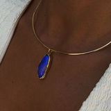 A close-up of a person's neck and chest wearing a delicate gold chain necklace with an irregular, polished blue stone pendant.