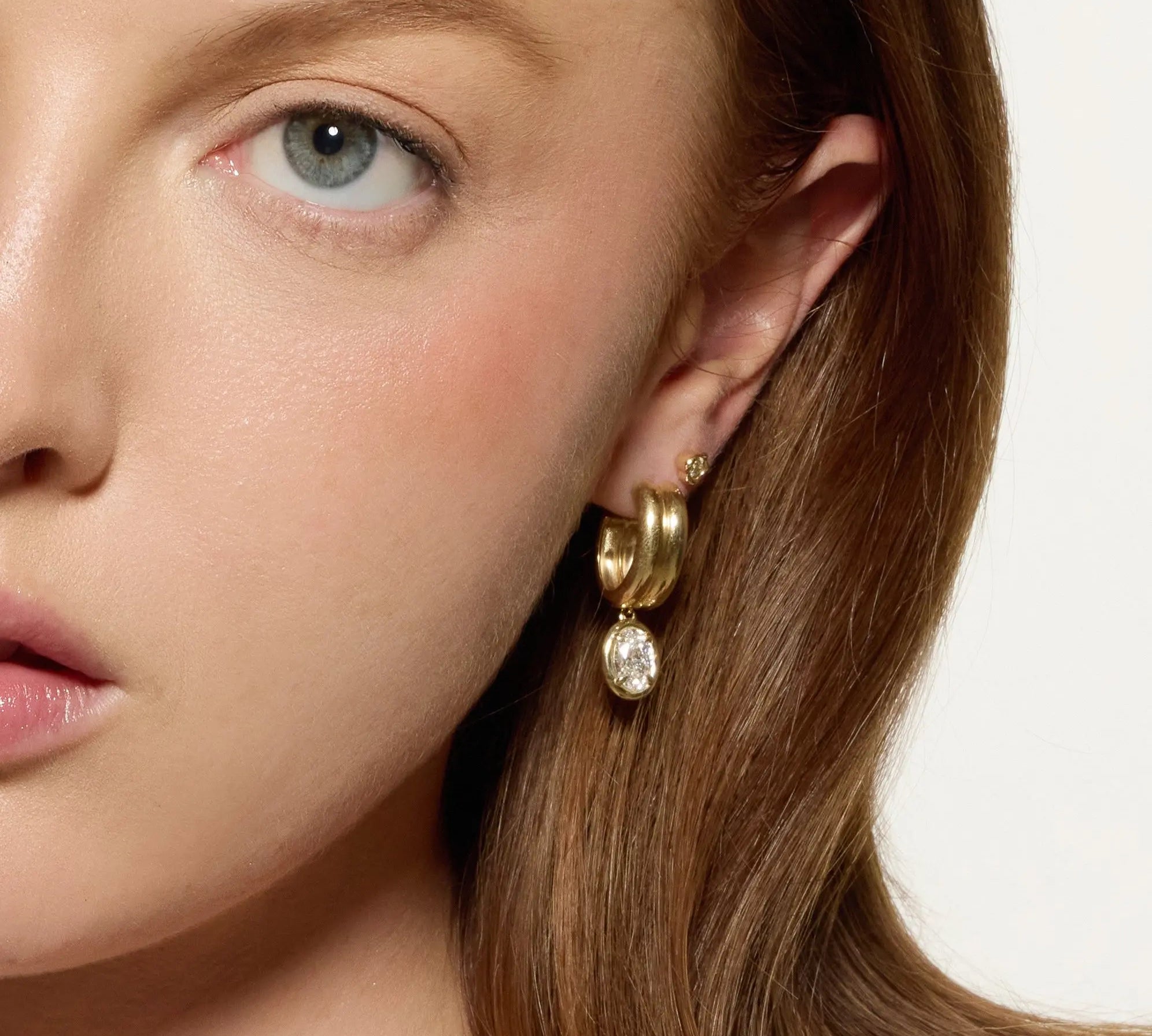 Close-up of a woman wearing gold hoop earrings with a white background