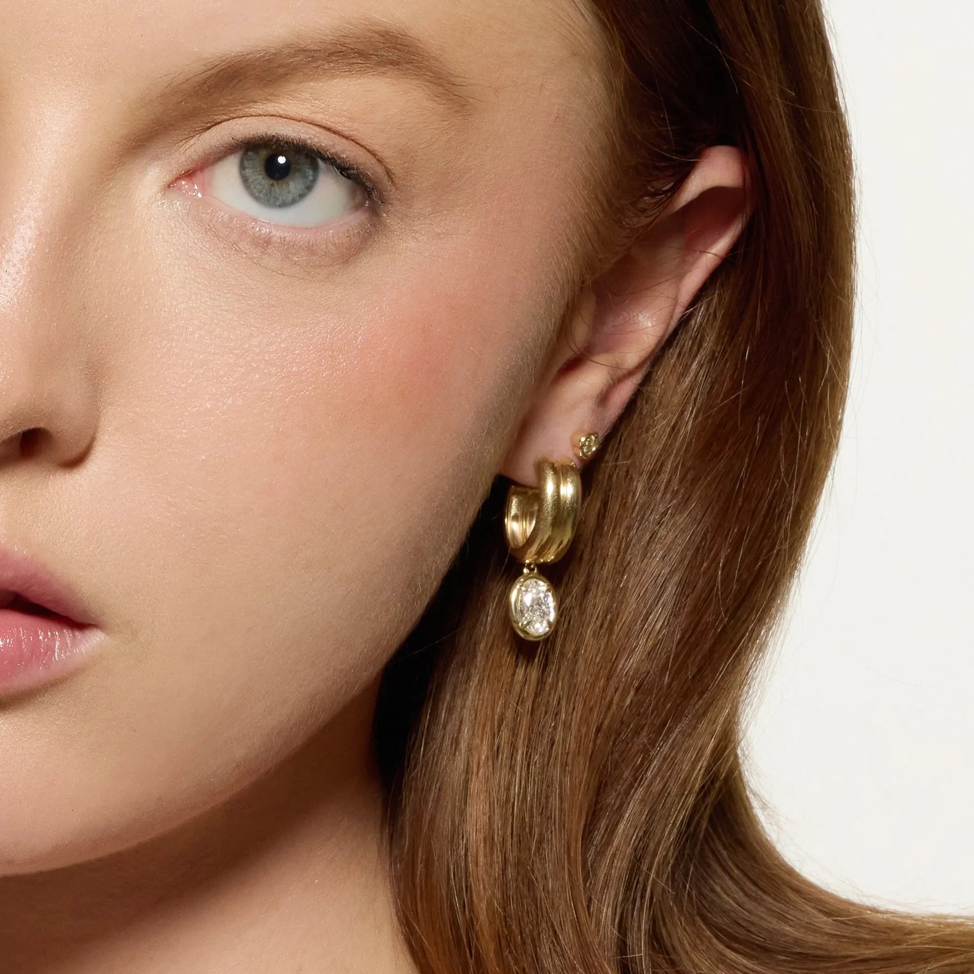 Close-up of a woman wearing gold hoop earrings with a white background