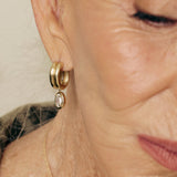 Close-up of a person wearing gold hoop earrings with a neutral background