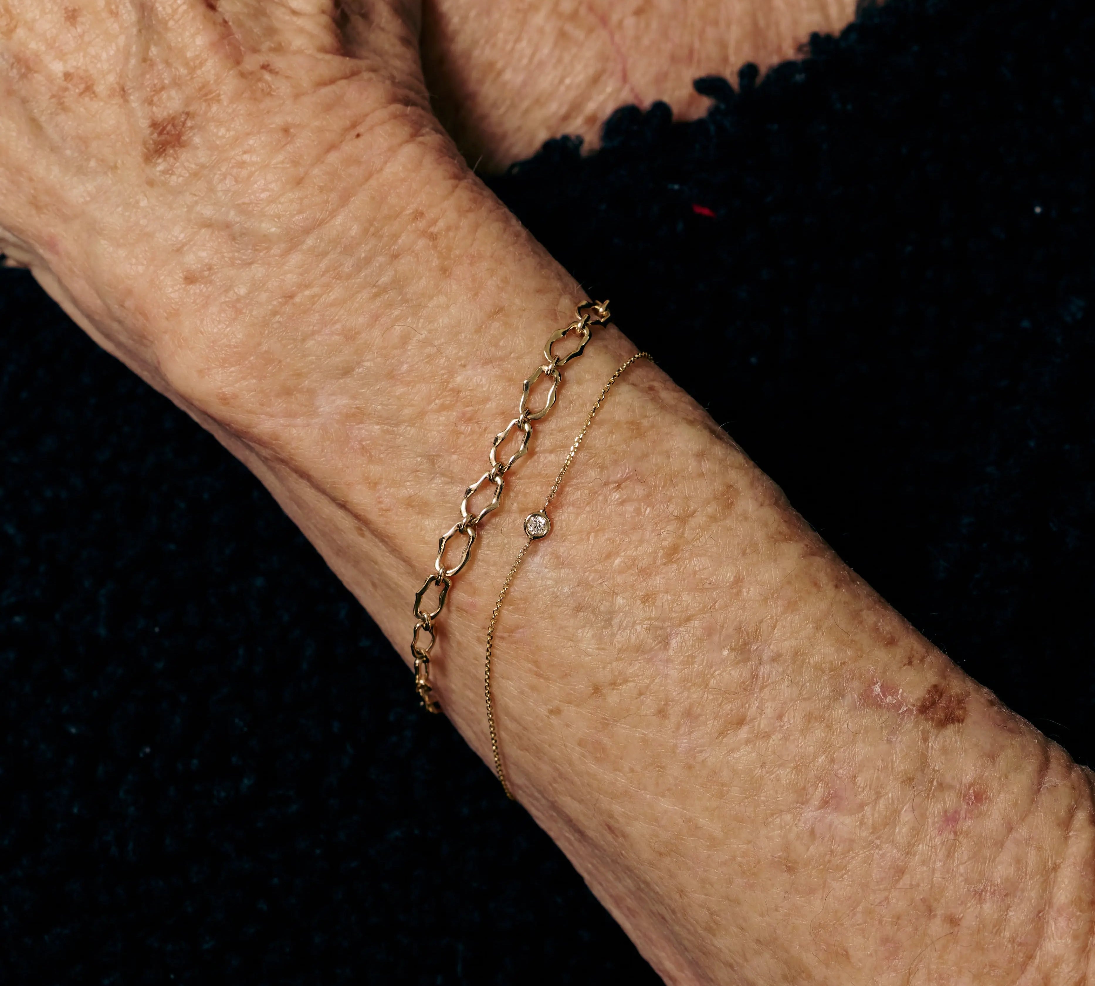 Close-up of an elderly person's wrist with a gold bracelet on a black background
