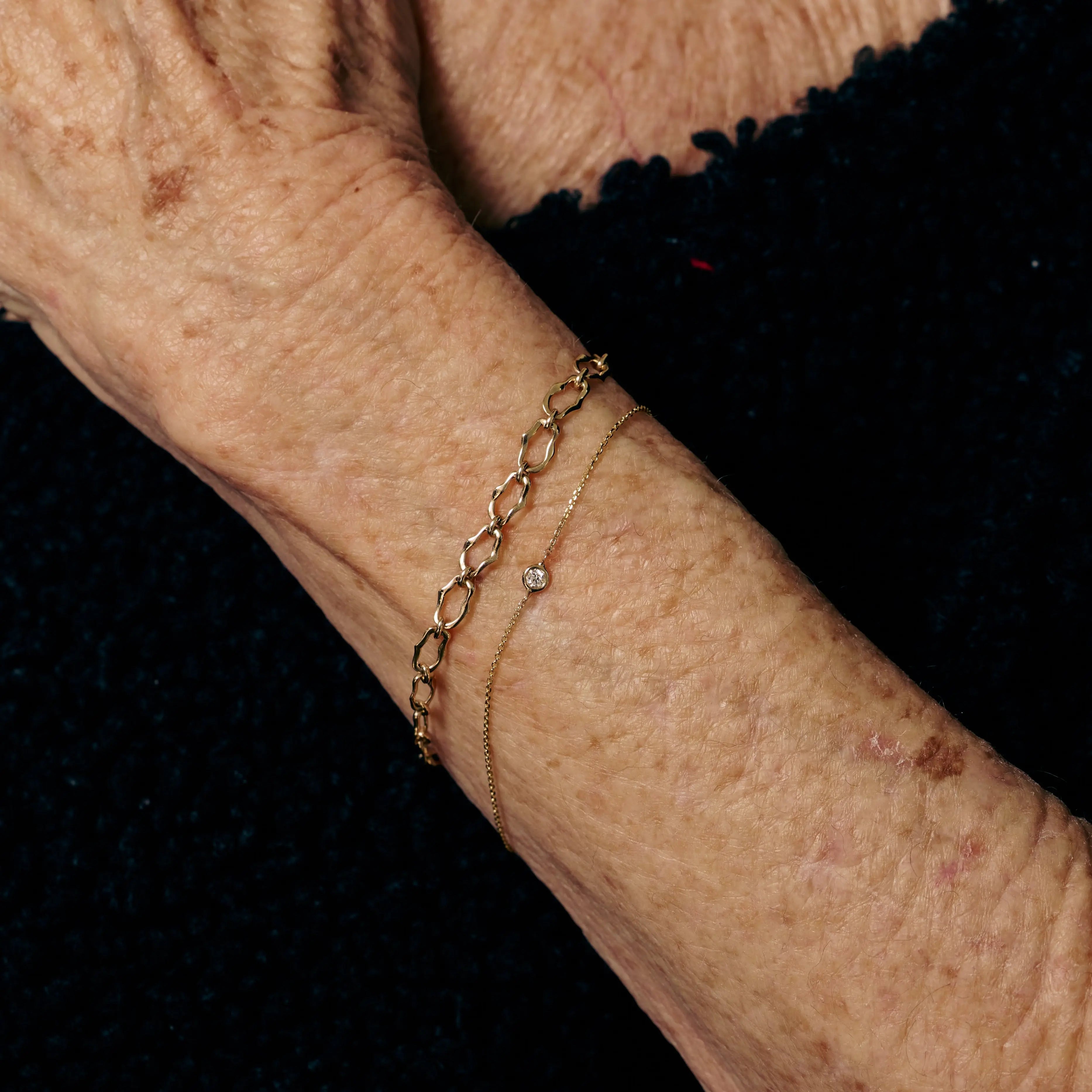 Close-up of an elderly person's wrist with a gold bracelet on a black background