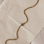 A close-up of a gold chain bracelet with a single round bezel-set diamond, laid diagonally across a textured beige surface.