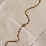 A close-up of a gold chain bracelet with a single round bezel-set diamond, laid diagonally across a textured beige surface.