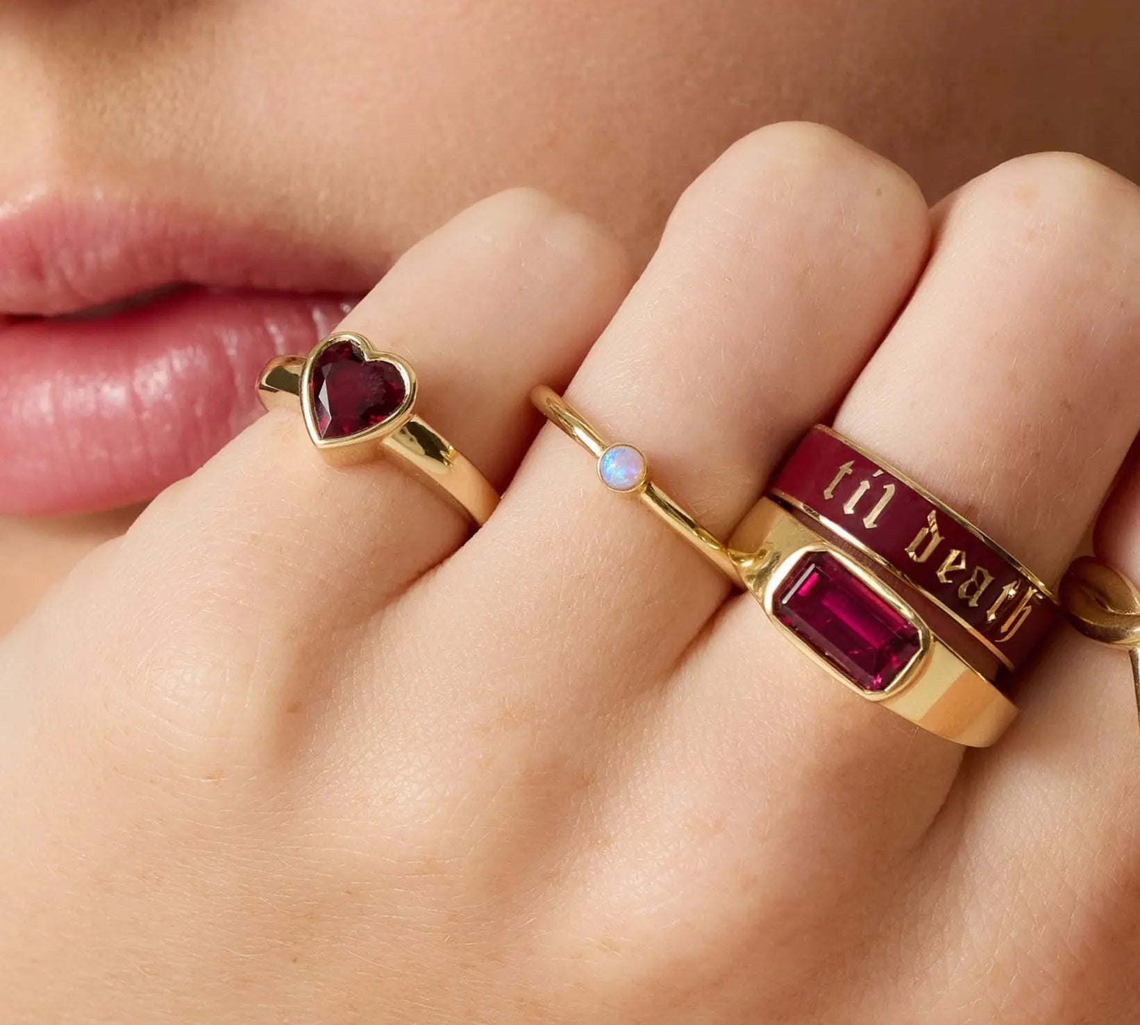 Close-up of a hand wearing multiple gold rings with gemstones and text.