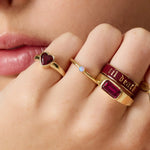 Close-up of a hand wearing multiple gold rings with gemstones and text.