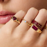 Close-up of a hand wearing multiple gold rings with gemstones and text.