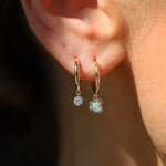 Close-up of an ear wearing gold hoop earrings with opal.