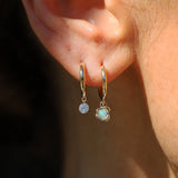 Close-up of an ear wearing gold hoop earrings with opal.