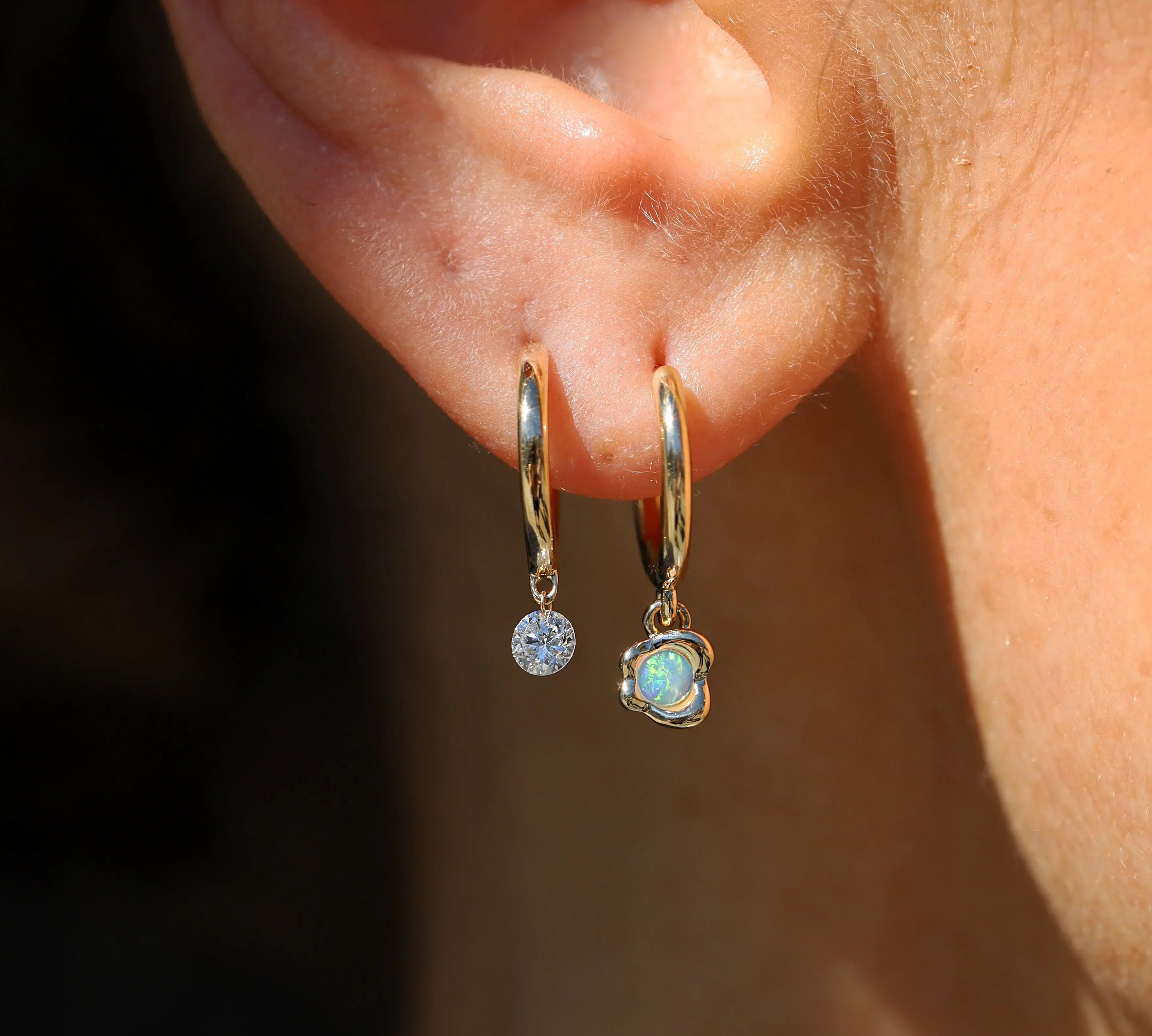 Close-up of an ear wearing gold hoop earrings with opal.
