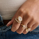 Close up of tilted pear diamond rind with diamond stacking band on hand with two other diamond rings