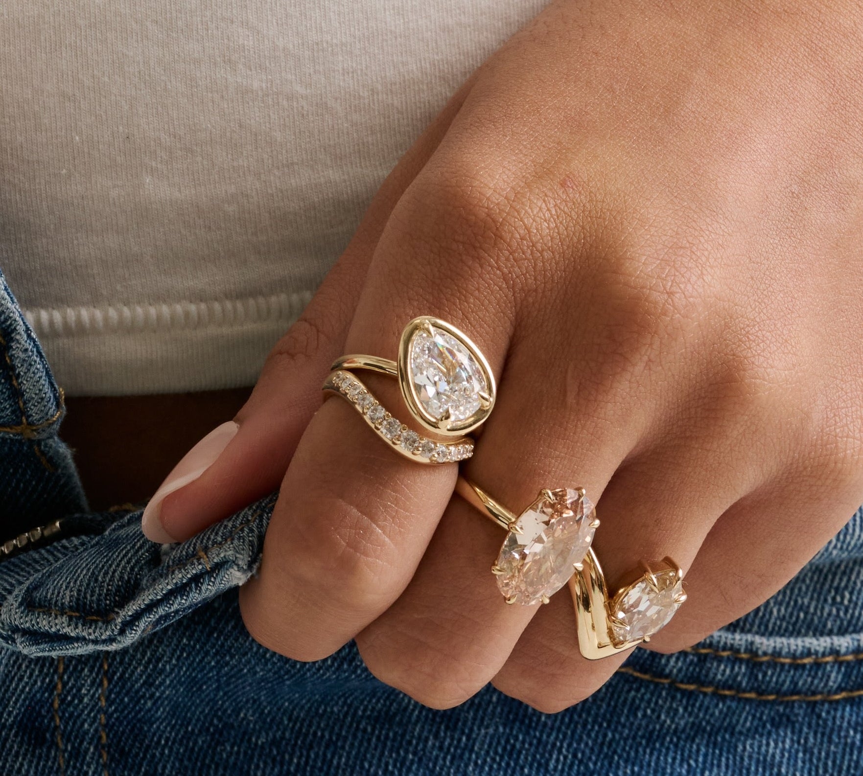 Close up of tilted pear diamond rind with diamond stacking band on hand with two other diamond rings