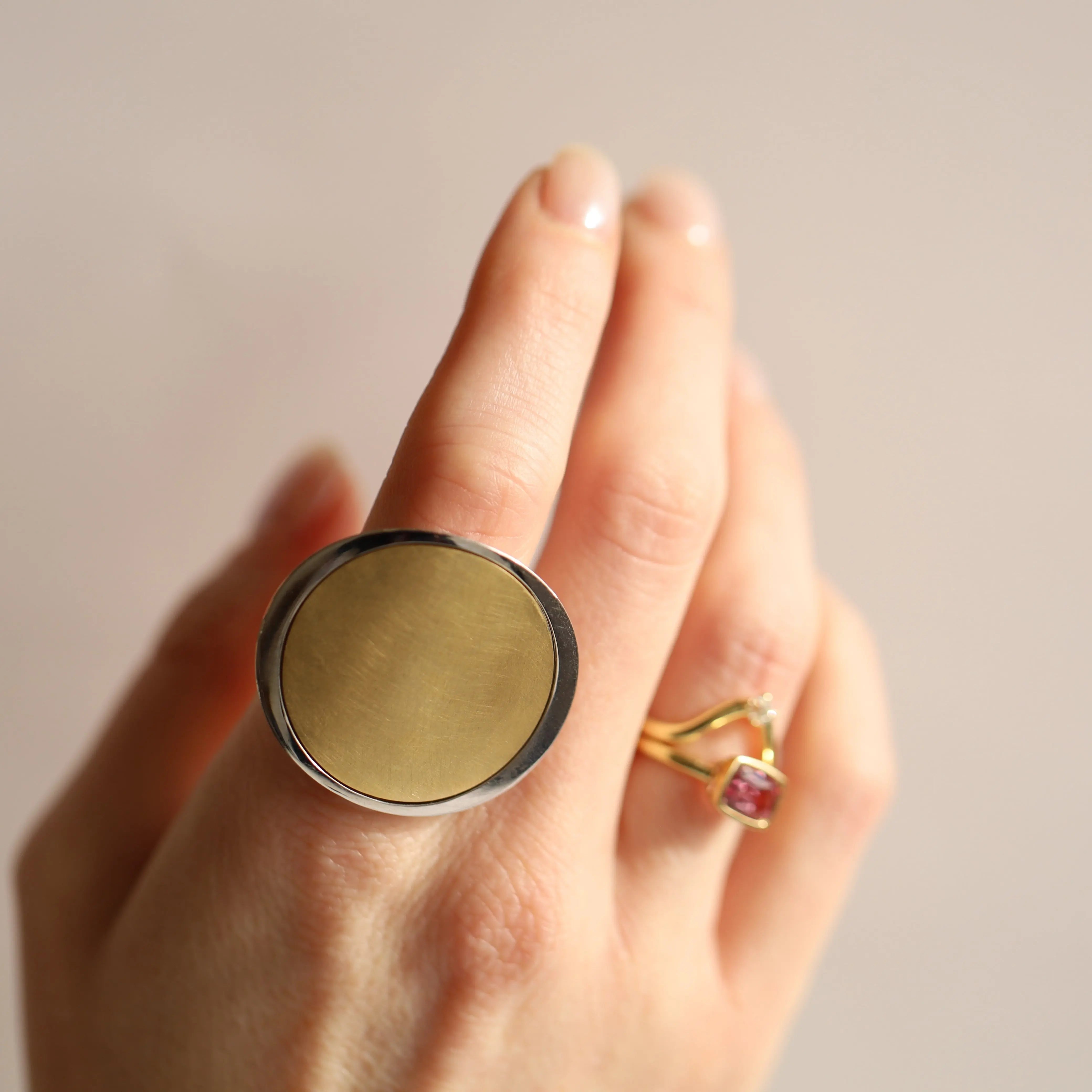 Hand wearing a large gold ring with a plain surface on a neutral background