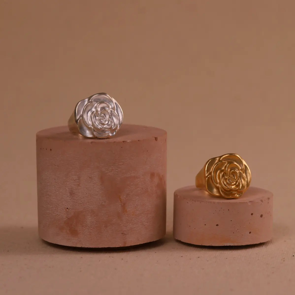 Two rings, one silver and one gold, on cylindrical pink stands against a beige background.