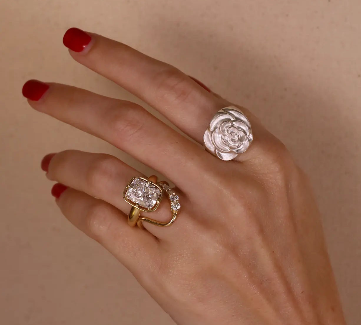 Hand wearing two rings with floral designs on a beige background