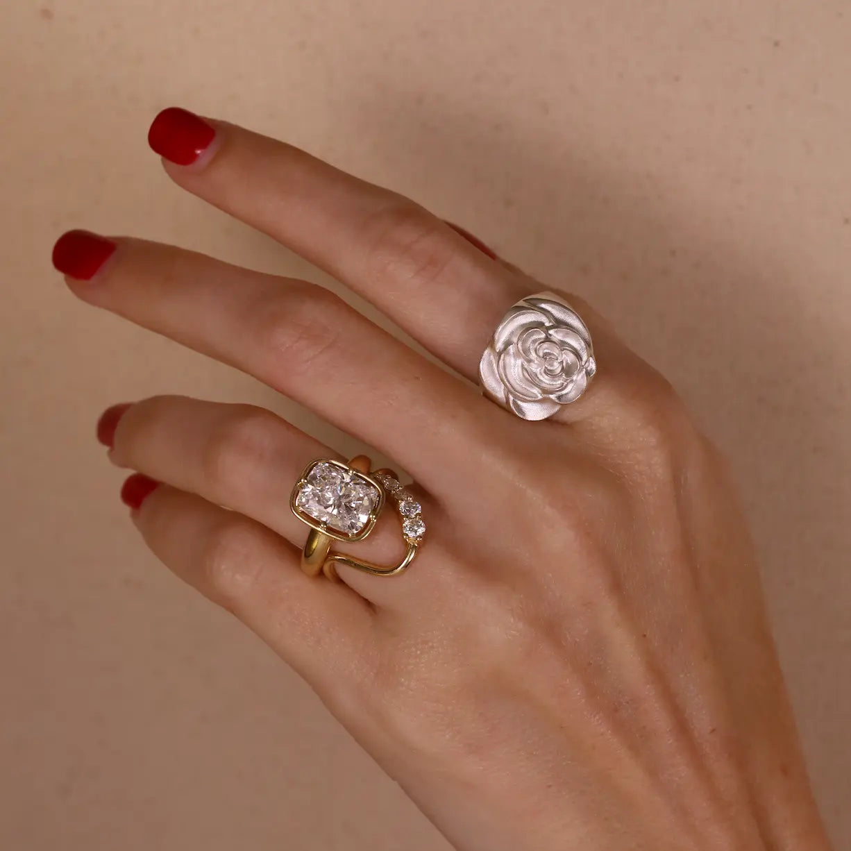 Hand wearing two rings with floral designs on a beige background