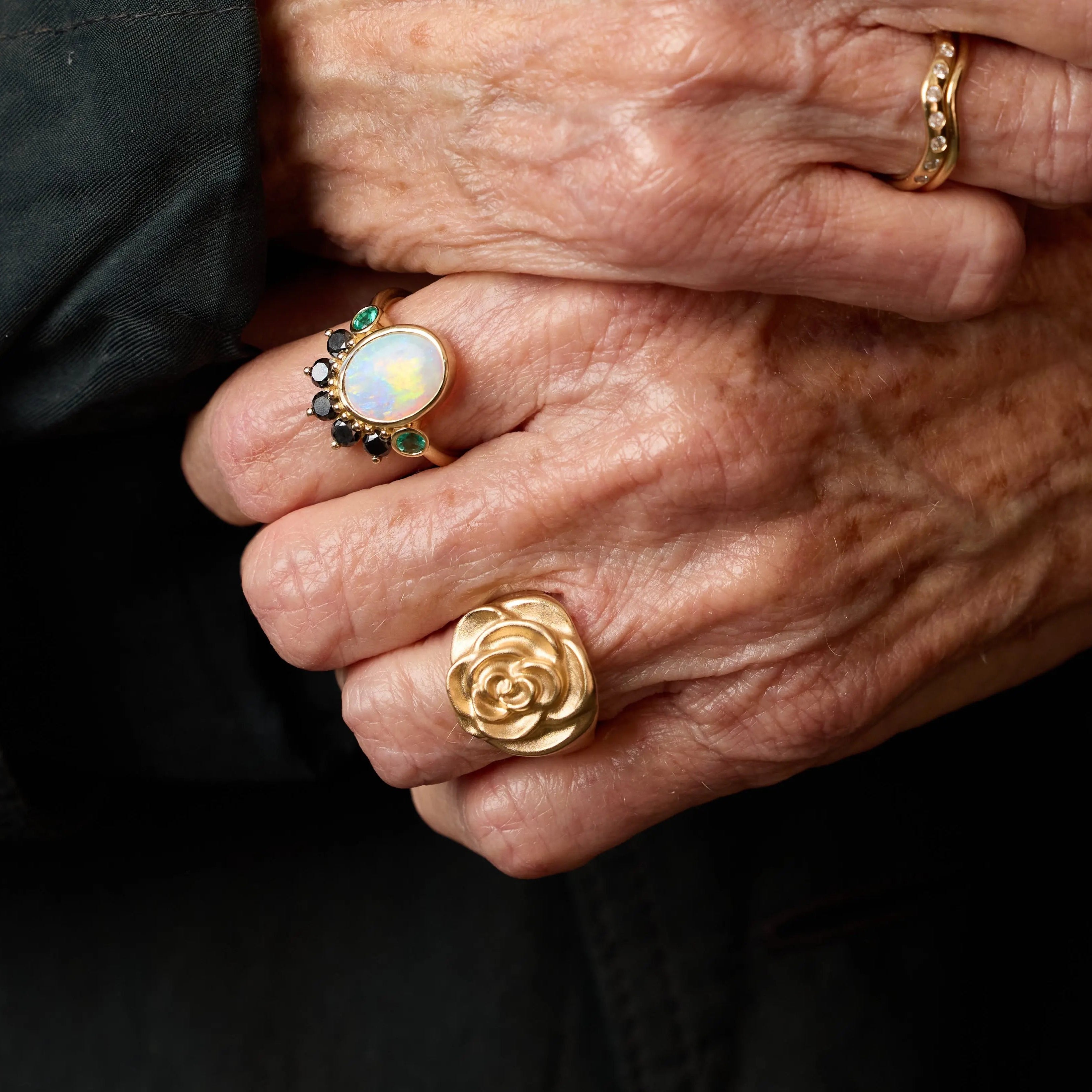 Close-up of hands wearing gold rings with a dark background