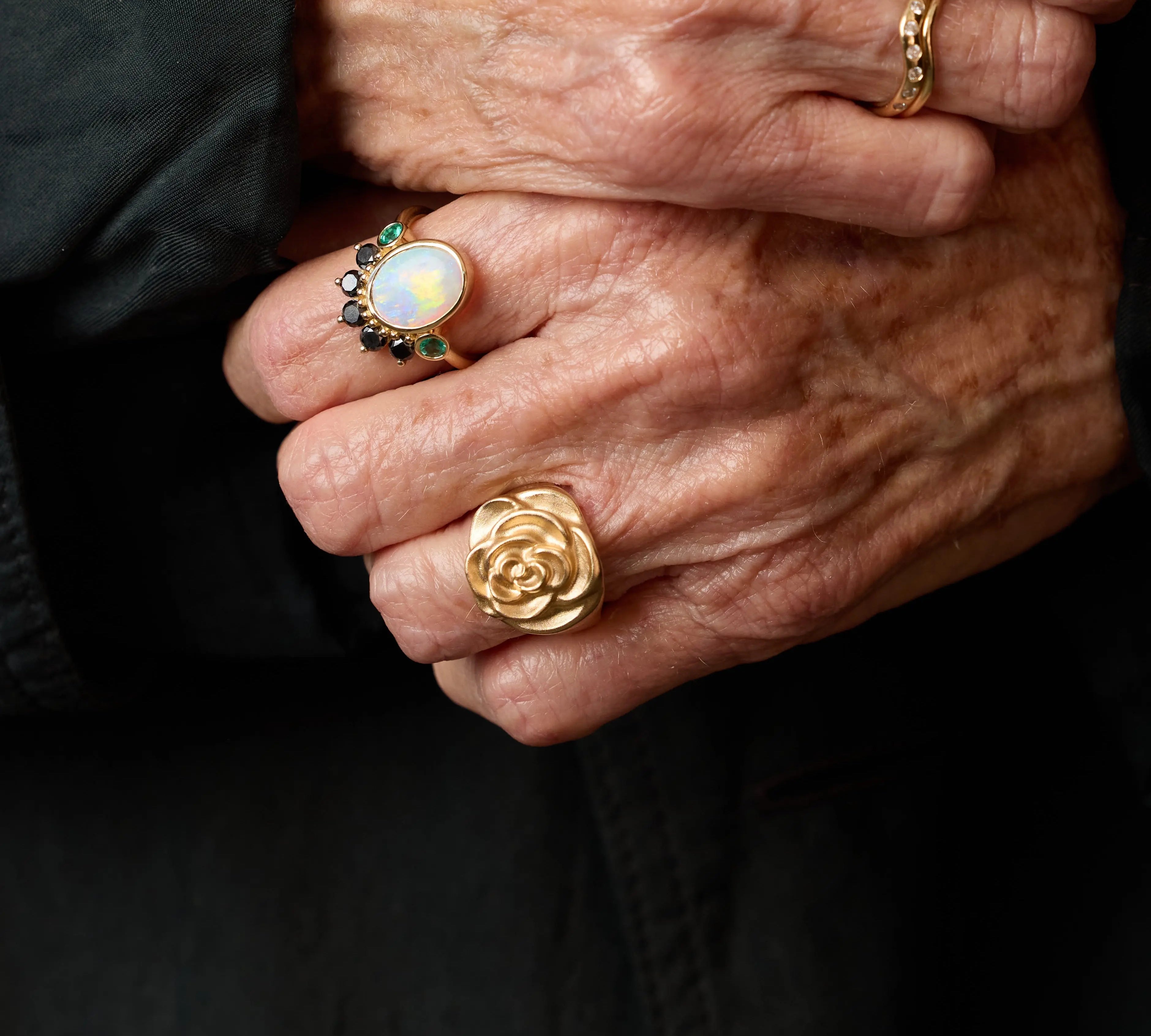 Close-up of hands wearing gold rings with a dark background