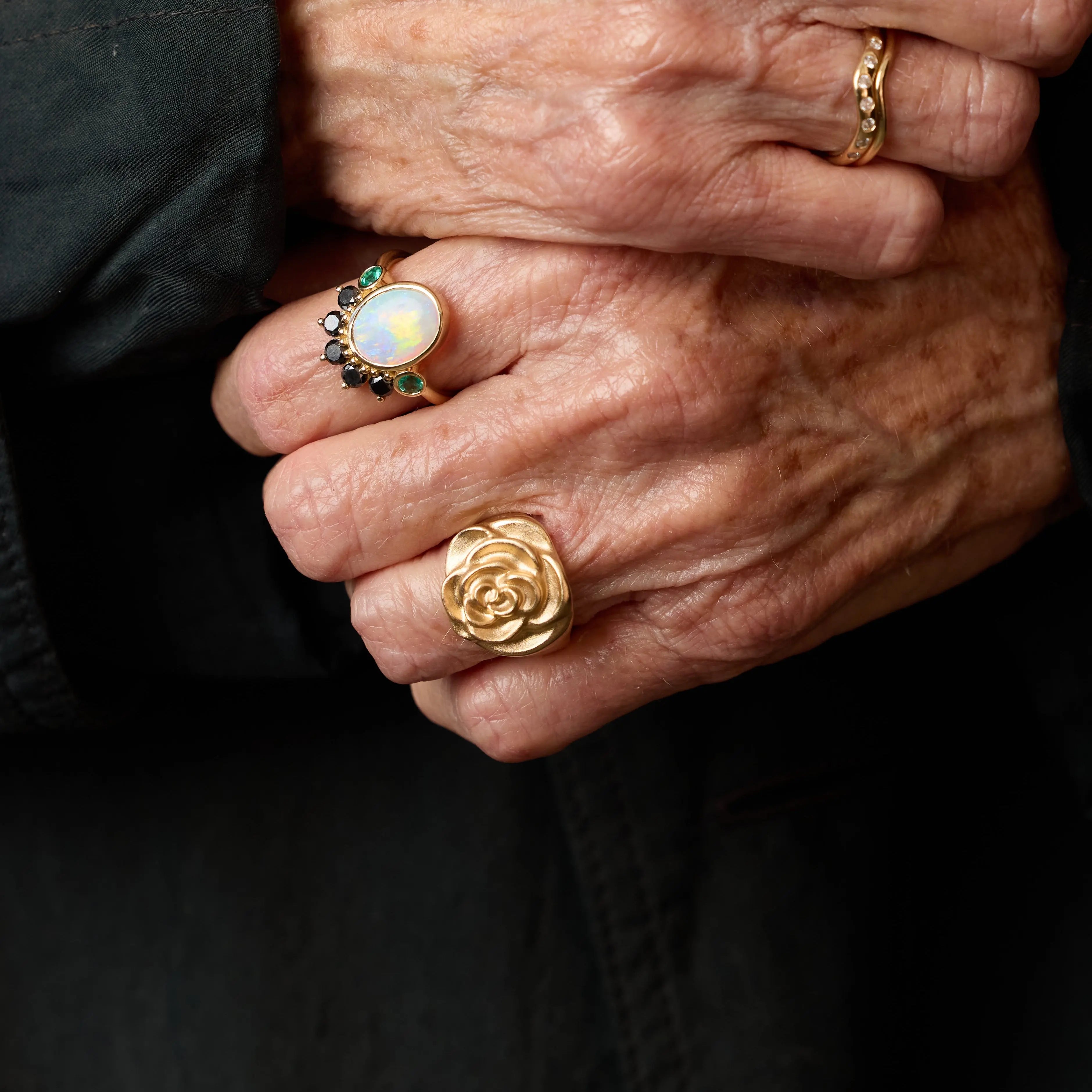 Close-up of hands wearing gold rings with a dark background