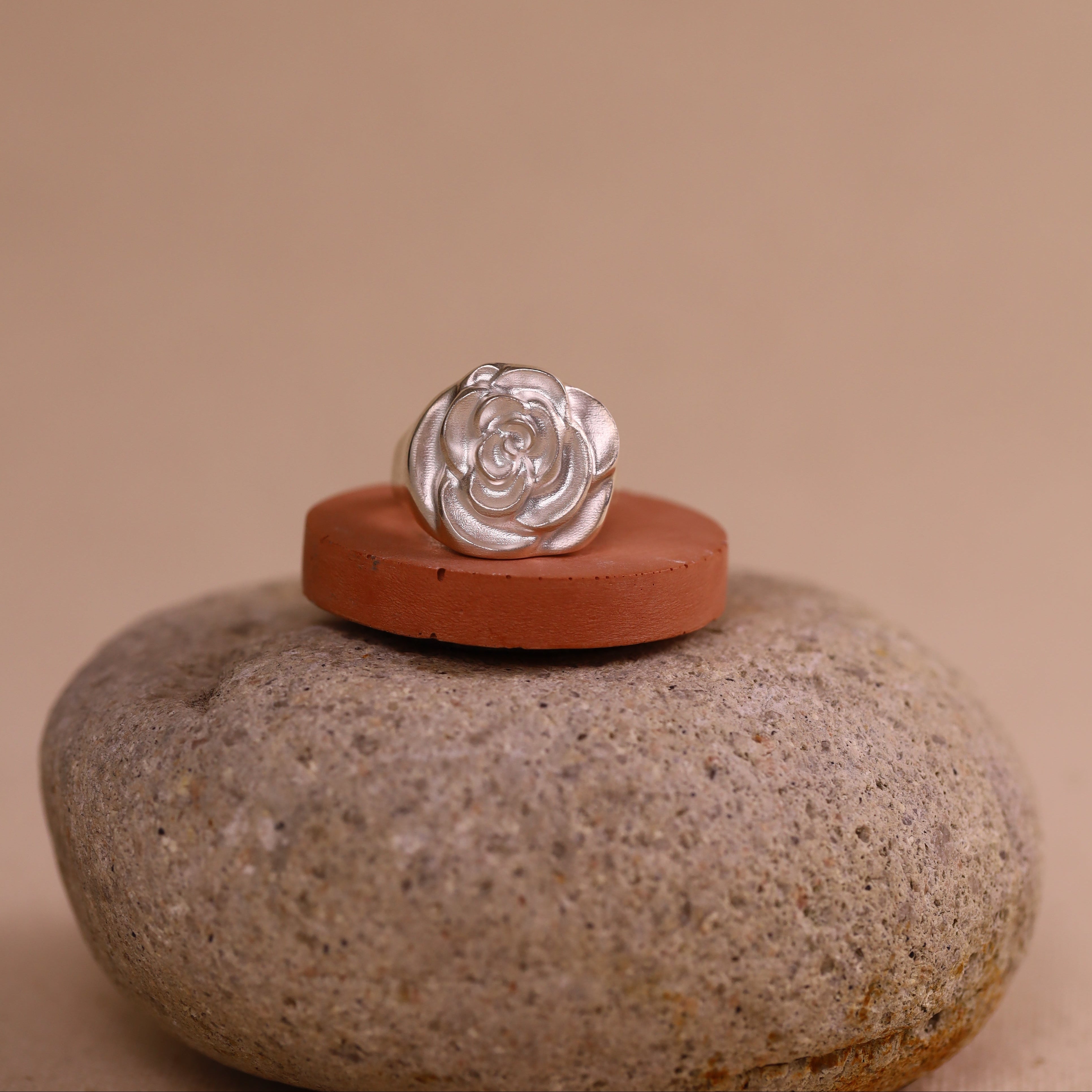 Silver ring with a rose design on a red stone with a beige background