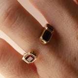 Open shank yellow gold and garnet band with subtle milgrain bezel detail on woman's hand against neutral background