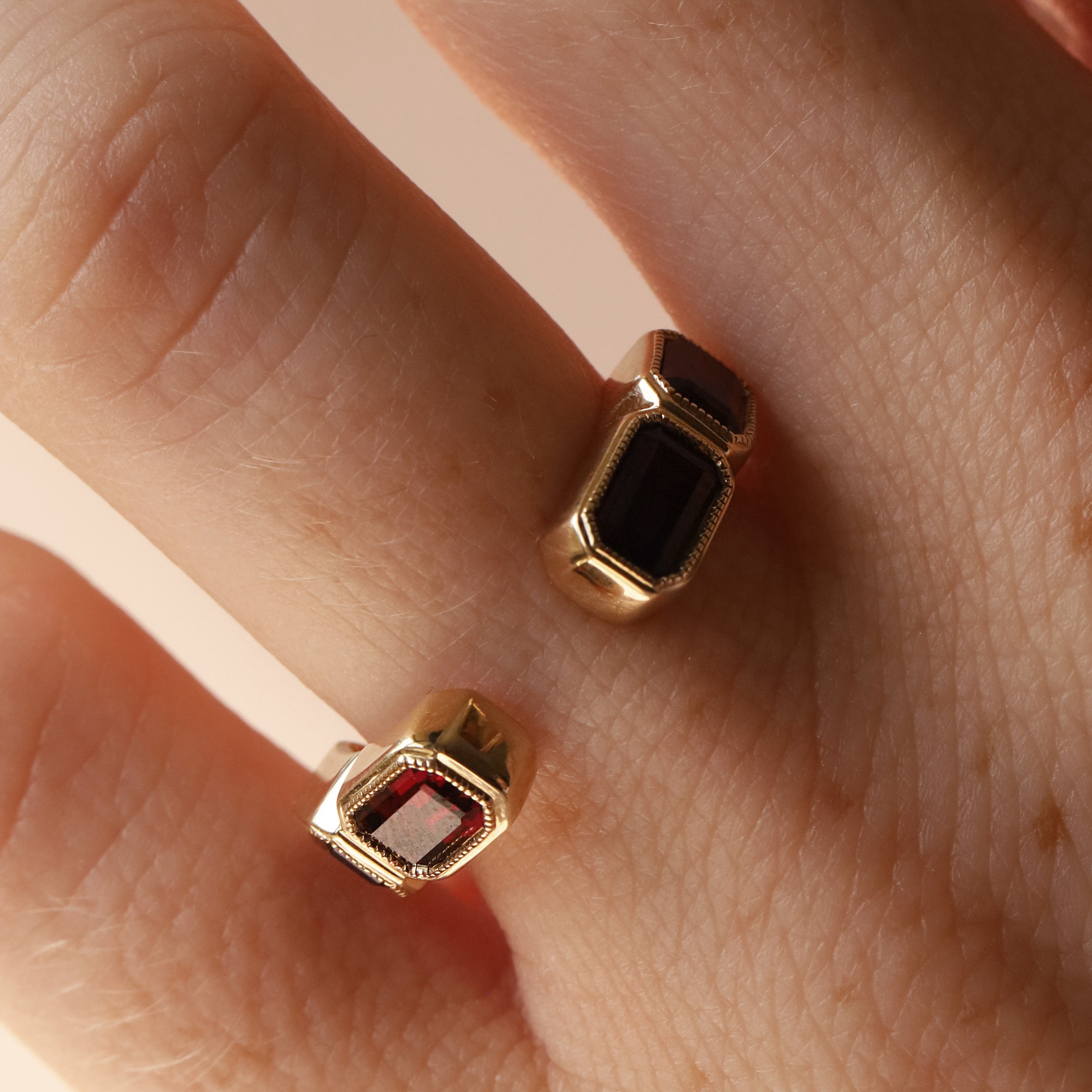 Open shank yellow gold and garnet band with subtle milgrain bezel detail on woman's hand against neutral background
