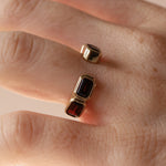 Open shank yellow gold and garnet band with subtle milgrain bezel detail on woman's hand against neutral background