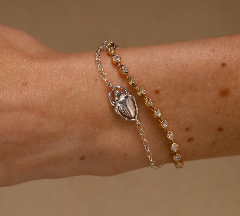 Bracelet with a scarab charm on a wrist against a beige background