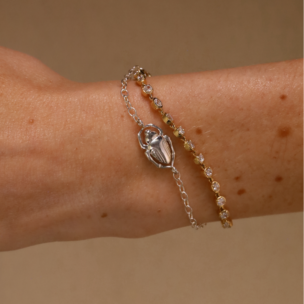 Bracelet with a scarab charm on a wrist against a beige background